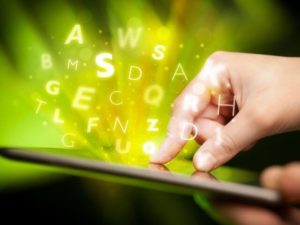 Close-up on a hand touching a tablet, with a bunch of letters floating off of it.