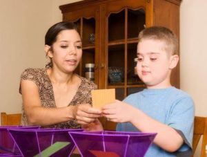 An adult and a child sitting in wooden chairs and looking at a orange post-it note they are both holding.