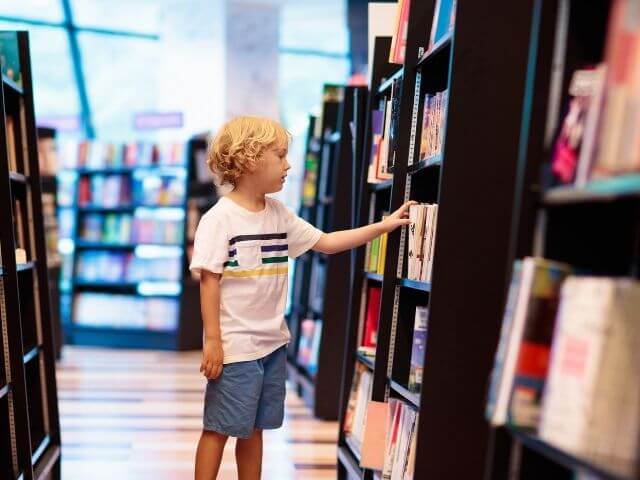 Kid in a white striped shirt, grabbing a book off of a bookshelf.