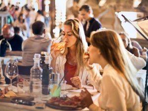 Person sitting at a table in a restaurant, drinking from a glass with orange liquid in it.