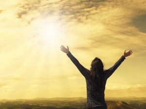 Someone in a grey shirt, reaching their hands out towards the cloudy sky.