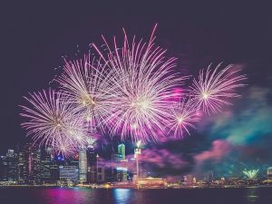 Purple and white fireworks over a cityscape set against a dark night sky.