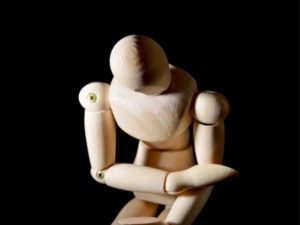 Wooden human figure doll with head slumped down and arms crossed as if hurting.