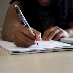 Close up on a person's hand holding a pen, writing on a notebook.