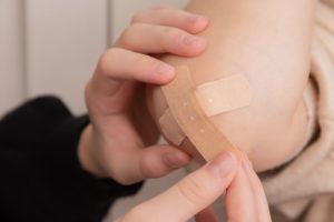 Close up of a hand putting two bandaids over a cut elbow.