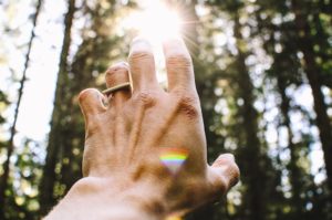 Closeup on a hand reaching towards sunlight that is peaking through trees.