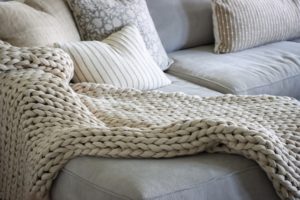 Big crochet blanket rested on a couch with monochromatic pillows.