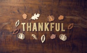 Wood background with the word "thankful" in the center, surrounded by stylized fall leaves and pumpkins.