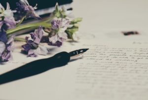 Purple flowers and a pen rested beside some paper.