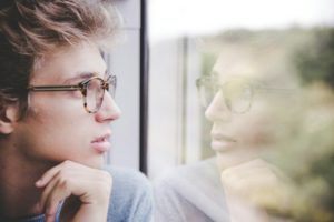 Close-up on a person looking through a window with their reflection looking back.