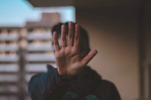 A hand being held up, covering the face behind it. Everything surrounding it is blurry.