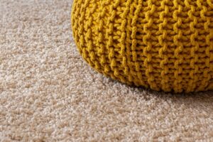 A yellow knitted bag on top of a fuzzy carpet.