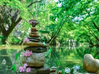 Stack of rocks with flowers and plants on on it. It's centered in the middle of water, and there's a bright forest around it.