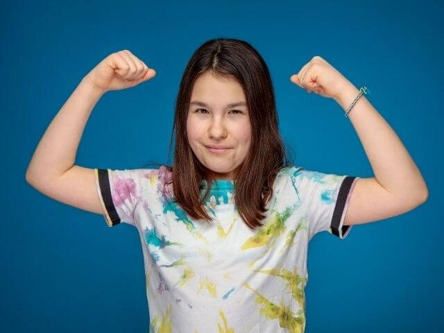 Yong person in a tie dye shirt, flexing their arms.