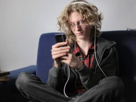 Person with curly hair, sitting on a dark grey couch and looking at a phone they're holding.