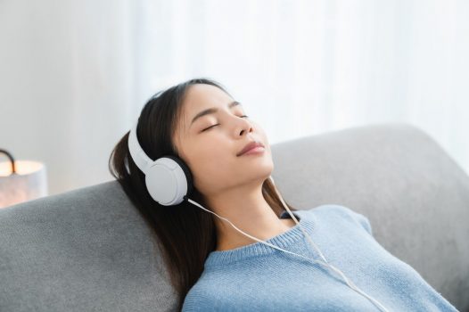 Person, in a blue shirt, wearing headphones and leaning back on a grey chair.