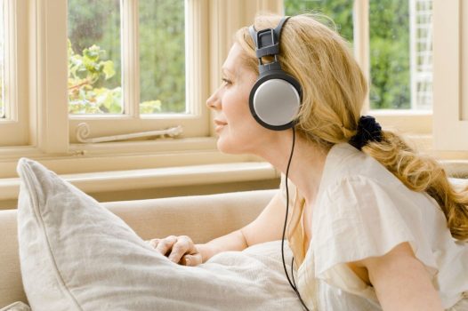 Person with long blond hair, in a ponytail, wearing headphone and looking out a window.