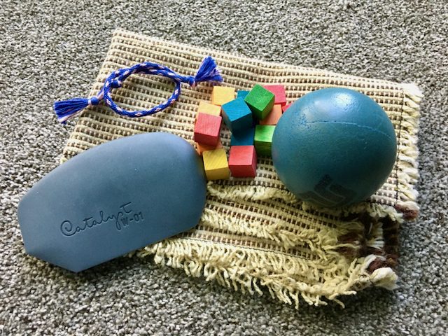 A blue ball, a few wooden blocks, a piece of rubber, string, and a folded piece of rough fabric, lying on gray carpet.