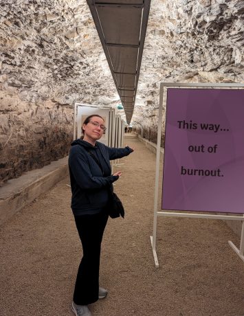 Leading out of burnout image A person in a blue hoodie gesturing towards a tunnel with a sign that reads, "This way... out of burnout."