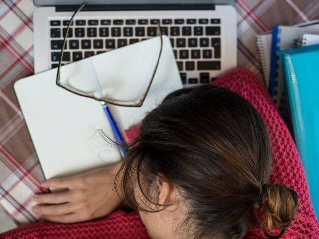 Close-up of a person laying their head down on their arms, which are rested upon a book.