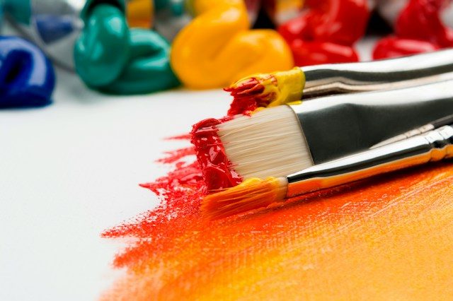 Paint brushes tipped with paint on an orange canvas.