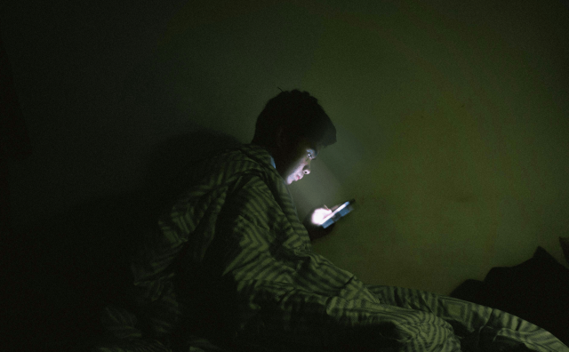 Person underneath a blanket staring at a bright phone in a dark room.
