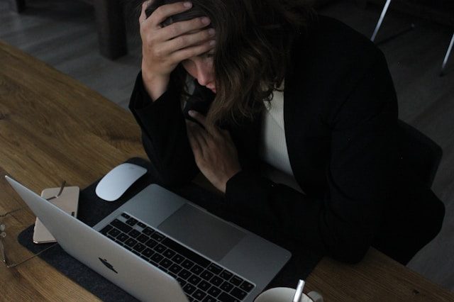 Woman with her hand on her head staring at a computer.