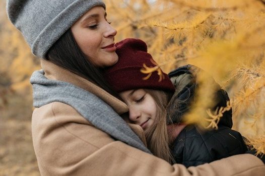 Close-up on two people, in jackets and hats, hugging.