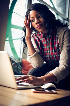 A woman pressing her hand against her forehead, looking down at the computer she's typing on.