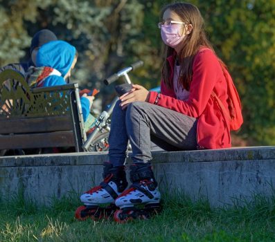 Person wearing a pink mask and roller blades, sitting on pavement above some grass.
