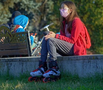 Person wearing a pink mask and roller blades, sitting on pavement above some grass.