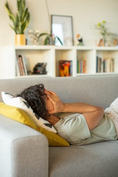 hrant-khachatryan-sIRLyJV8ooA-unsplash A person laying on a couch, holding their hands over their face.