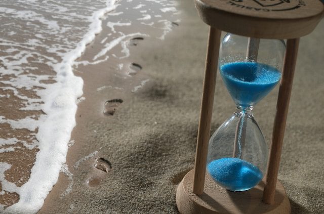 Hourglass rested on the shore nearby footprints.
