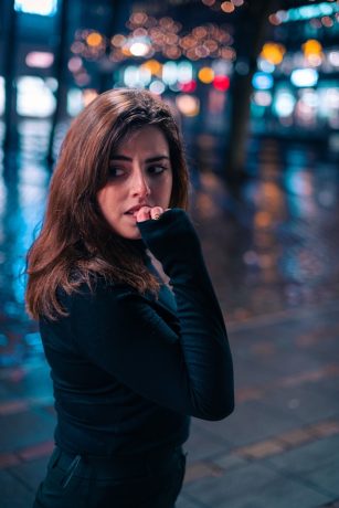 khaled-ali-QlGKsnSwCLs-unsplash Person chewing on their fingernail in front of blurred city lights.