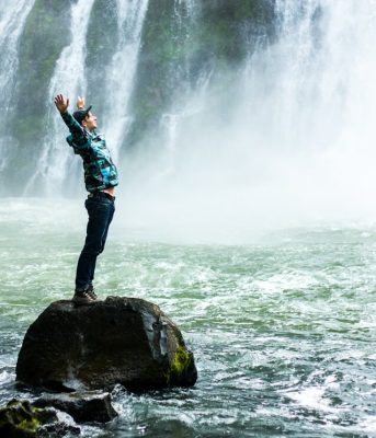 slav-romanov-r38u2Uq1AXk-unsplash Someone stretching on a rock while looking towards a waterfall.
