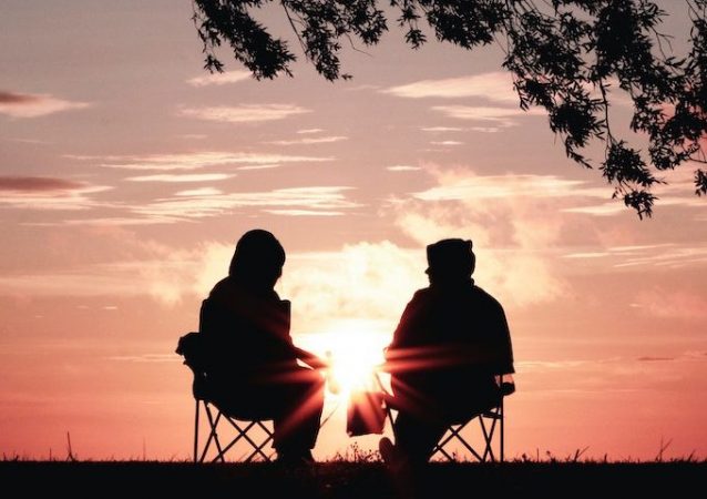 Silhouette of two people sitting on chairs in front of a sunset.