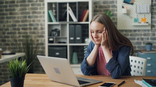 Person with their head in their hands, staring at the computer in front of them.