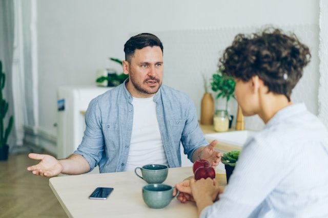 Distraught man talking to someone across a wooden table.